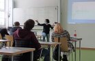 Mehrere Personen sitzen mit Abstand in Klassenzimmer